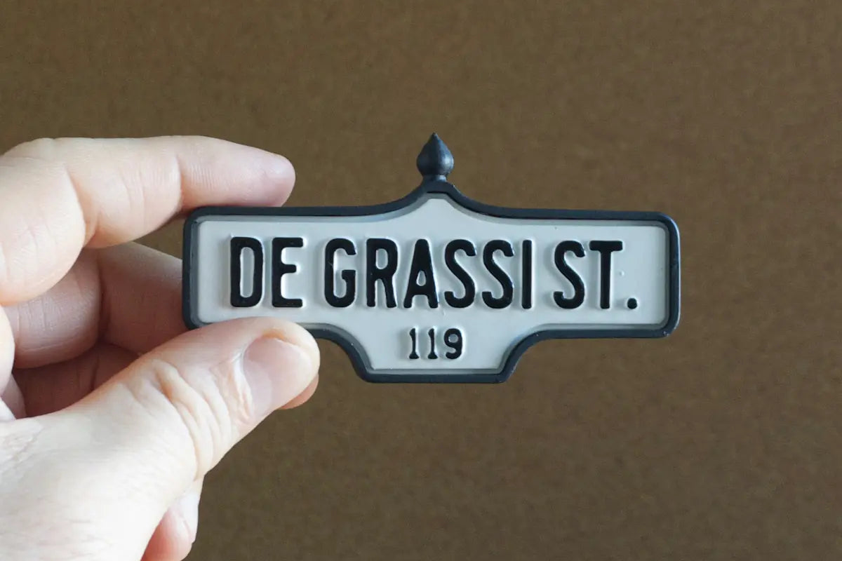 In-hand view  of De Grassi St. #119 Pin - Standard Finish, miniature replica Toronto acorn street sign