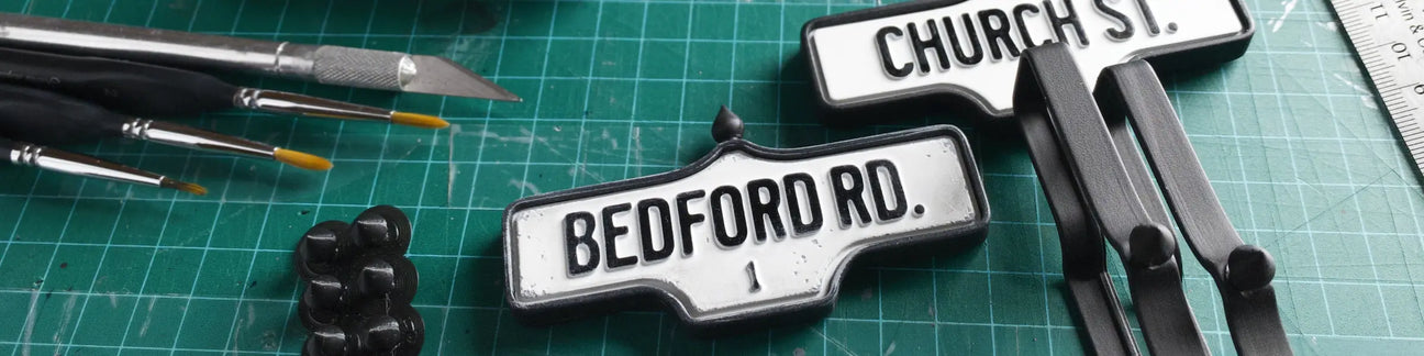 Two acorn street signs: Church St. and 1 Bedford Rd. on a workbench with tools.